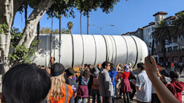 The crowd of onlookers watches as one of Endeavour's two solid rocket motors enters the premises at Exposition Park in Los Angeles...on October 11, 2023.