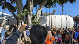 The crowd of onlookers watches as one of Endeavour's two solid rocket motors enters the premises at Exposition Park in Los Angeles...on October 11, 2023.