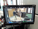 A playback monitor showing Noureen DeWulf and Eddie Jemison filming a scene for COFFEE, KILL BOSS