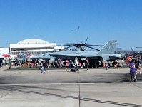 A UH-1 Iroquois, an F/A-18 Hornet and another C-130 are surrounded by crowds of people as an air demo takes place in the distance...on September 24, 2016.