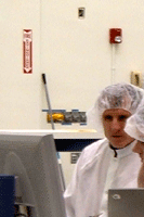 Two technicians at work within the Spacecraft Assembly Facility.  Behind them is a mannequin dressed in a blue clean suit.